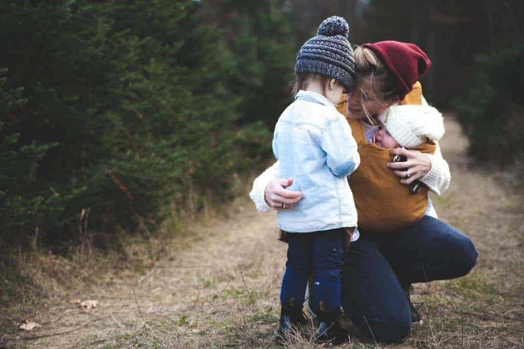 mom toddler and baby in winter hats outside hugging