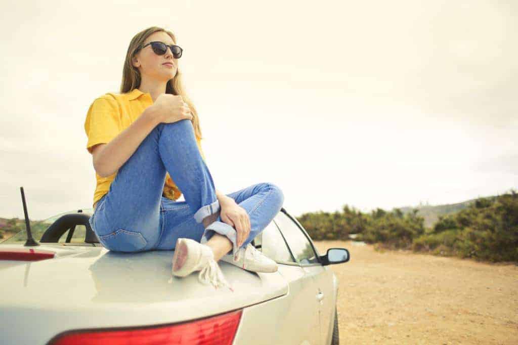 young womna in jeans sitting on top of a car