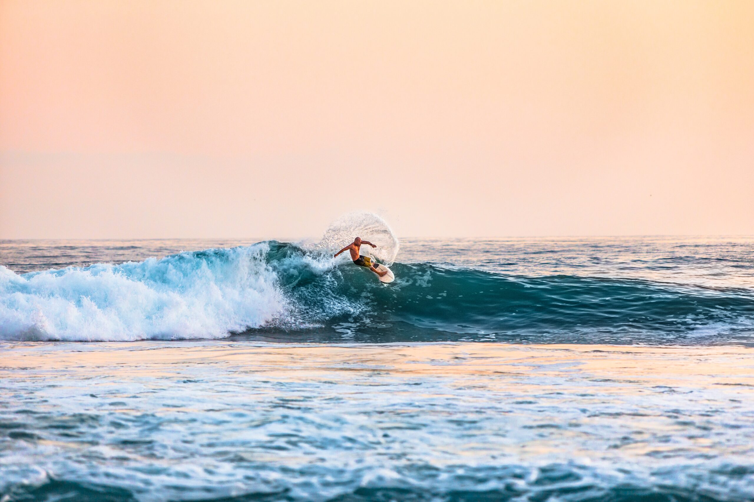 solo surfer on a blue wave with pink sky