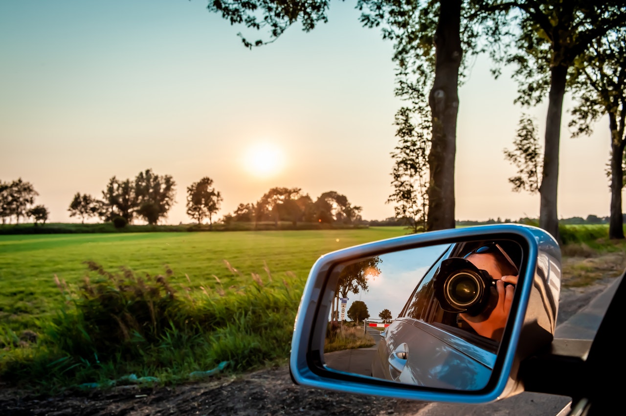 woman with point and shoot camera in car mirror on the road at sunset