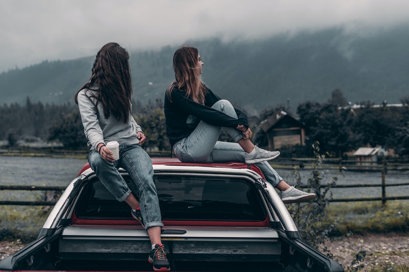 two women drinking coffee on top of a car